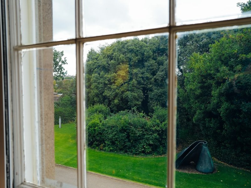 A large picture window looking out onto a lawn and mature trees
